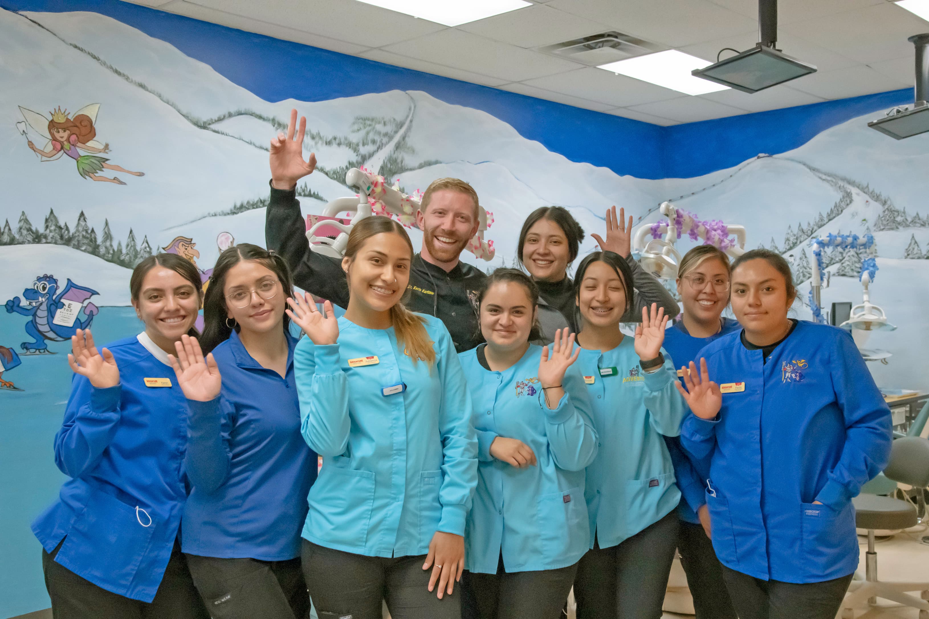 ten people wearing blue medical scrubs at a dental office waving and smiling
