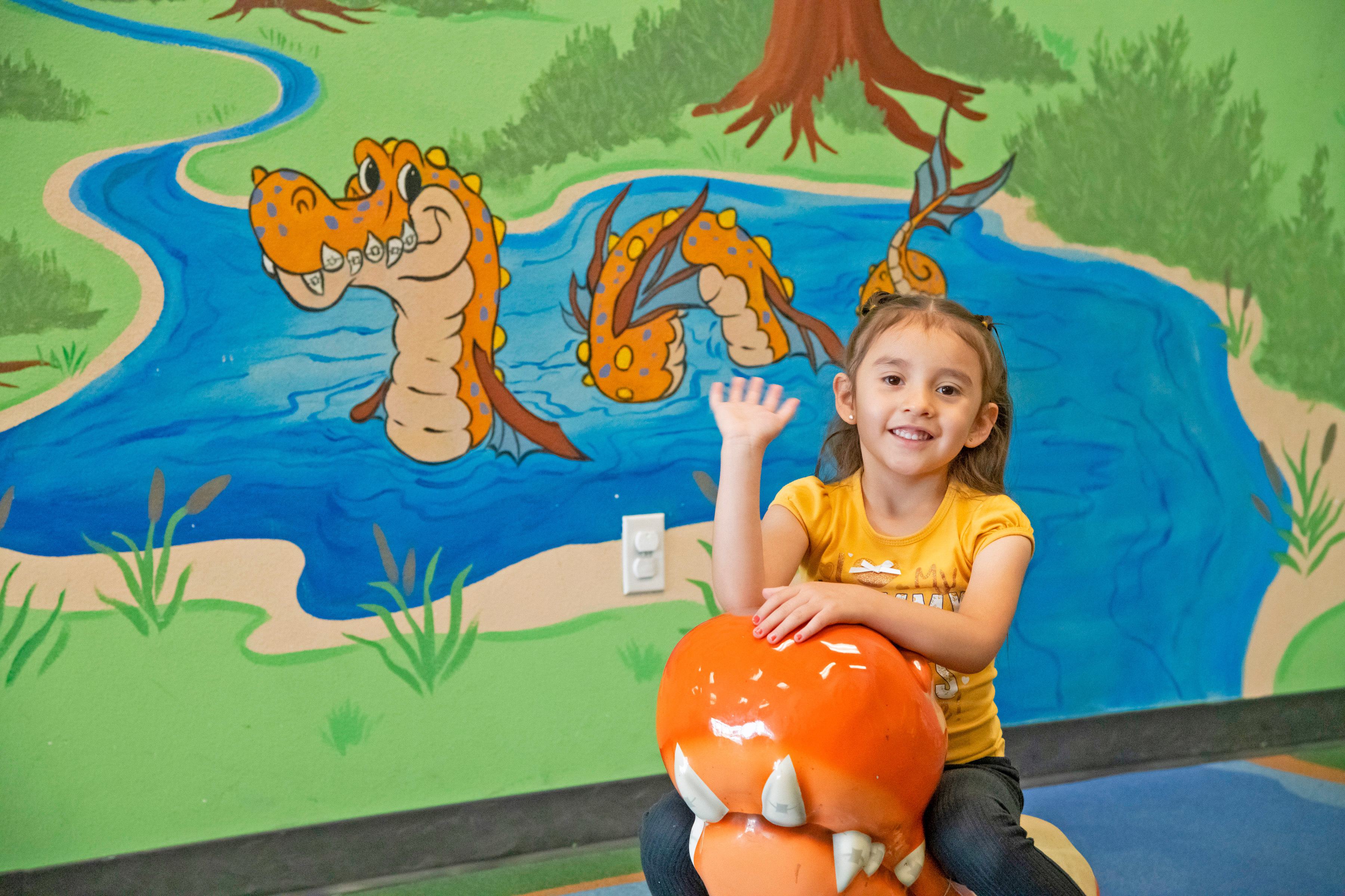 young girls sitting on an orange dragon waving and smiling