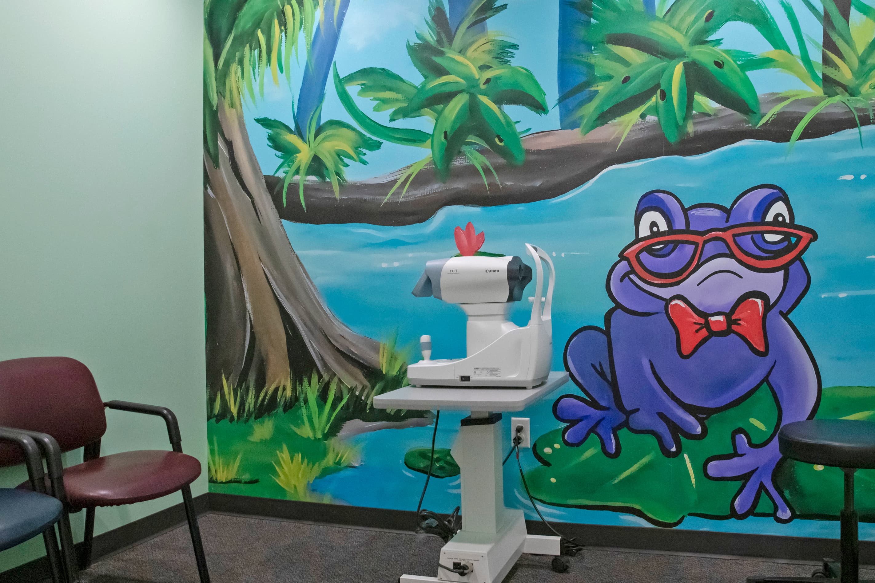 a wall mural in a vision exam room of a purple frog wearing red glasses
