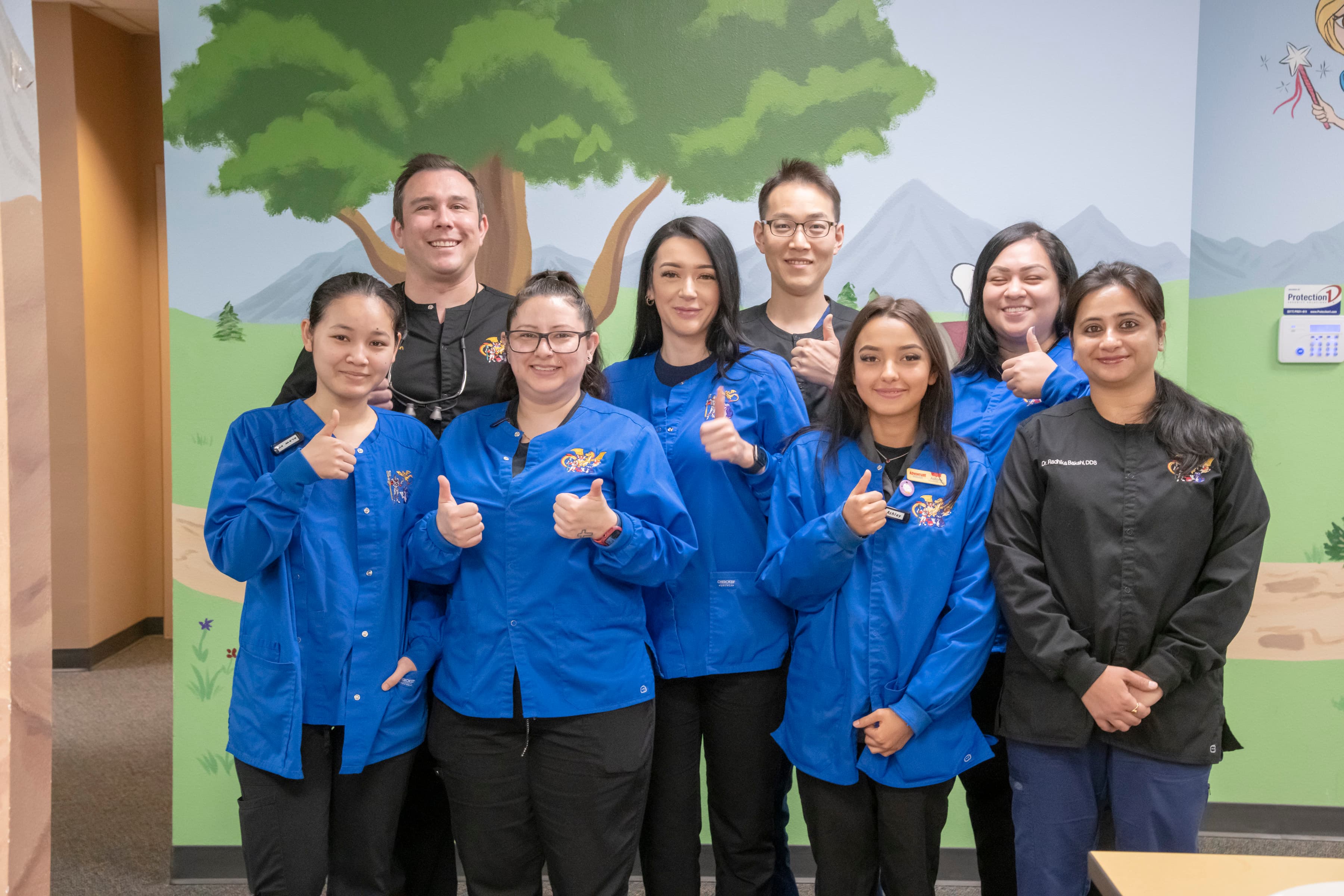 Pediatric Dental, vison and orthodontic staff at Aurora Adventure Dental location , eight people wearing blue medical coats, smiling and waving.