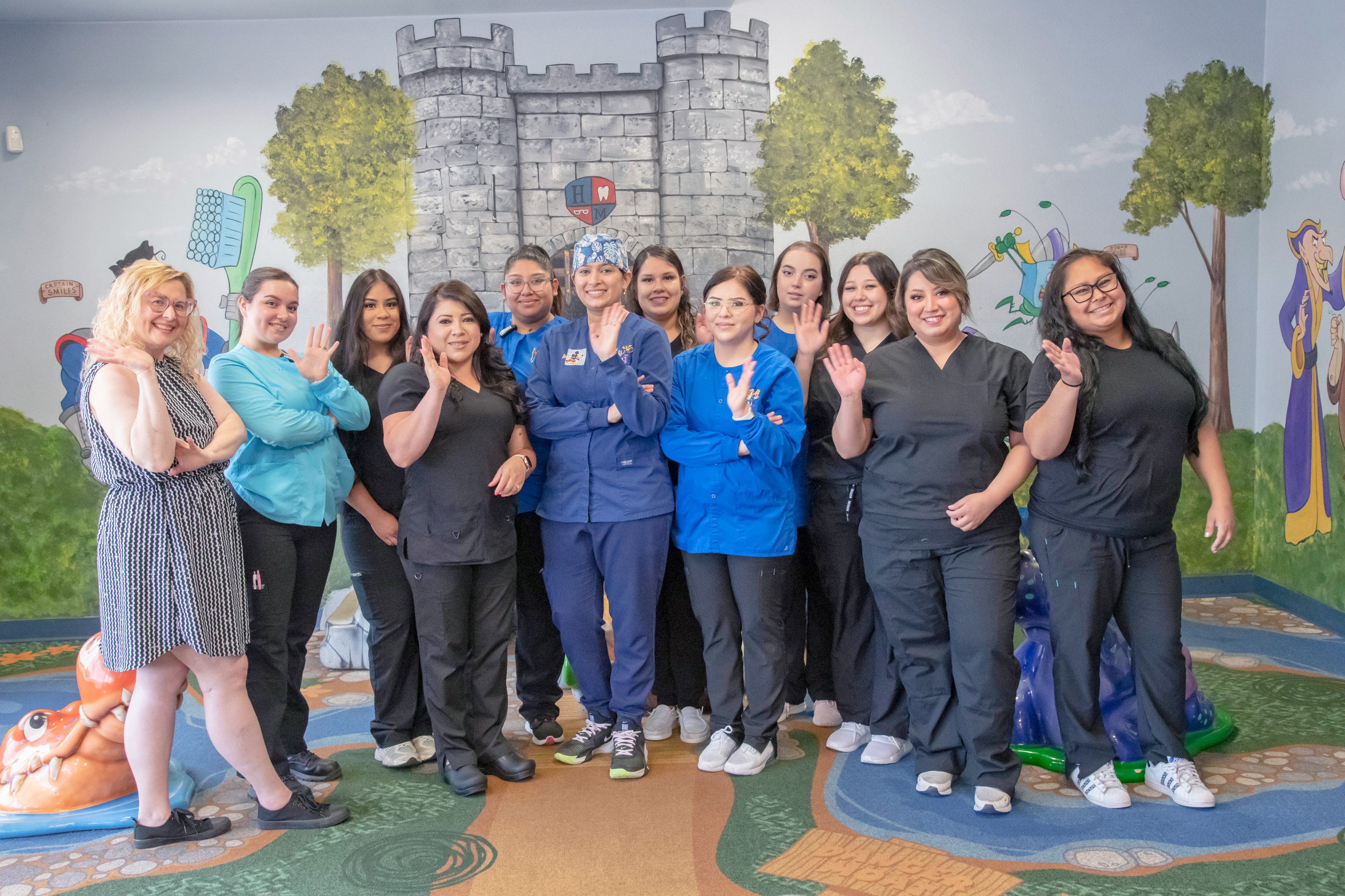 Pedatric dental, vision and orthodontic staff at our office in Greeley. Twelve people are wearing blue and black clothing. They are standing and smiling.