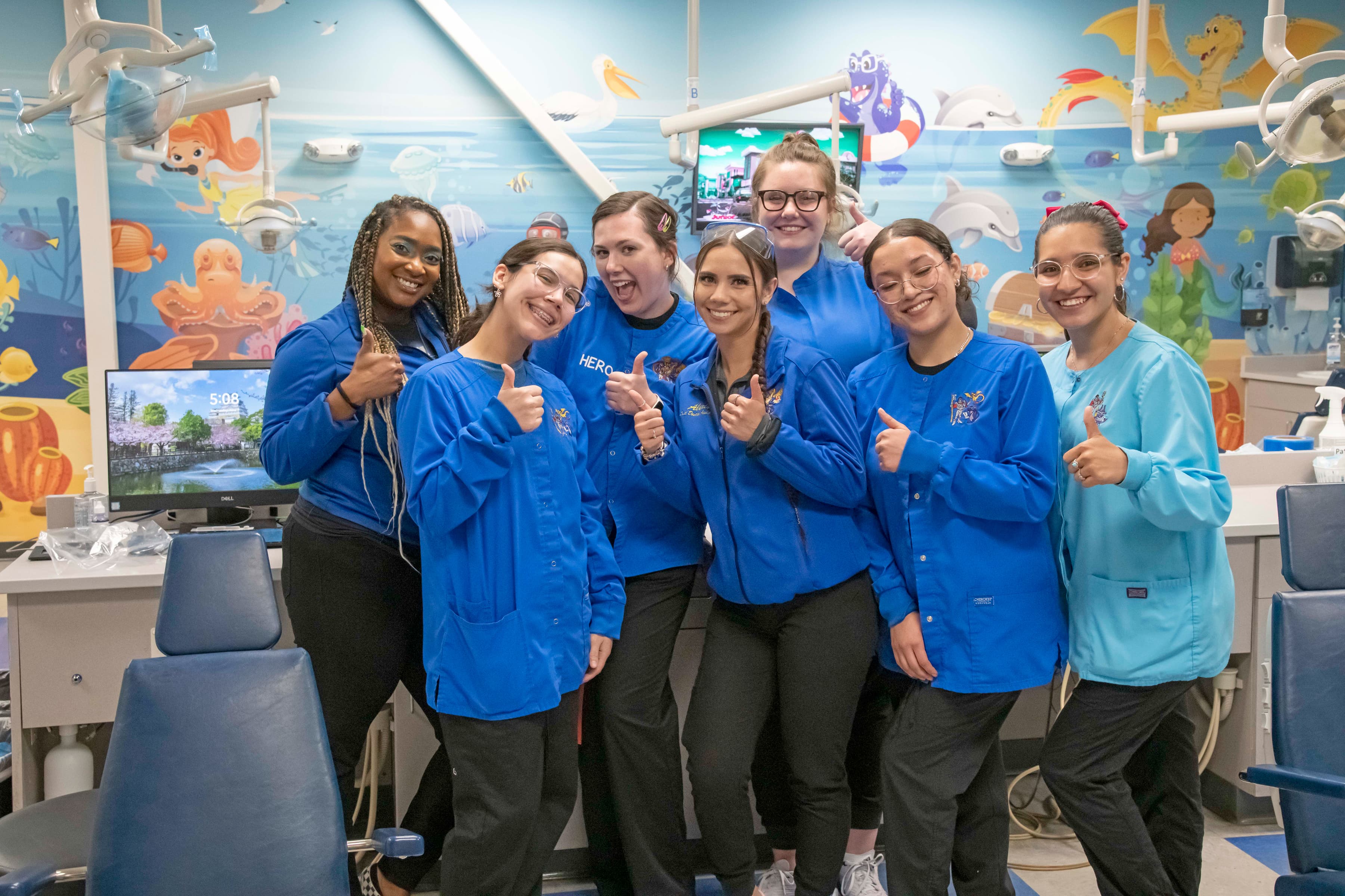 pediatric dental care and vision care staff of seven people at the north Colorado Springs office smiling and waving, wearing blue medical clothing